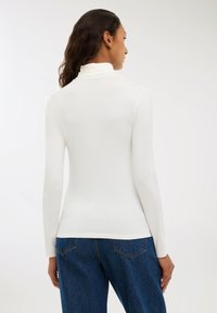 Maglietta bianca a maniche lunghe con scollatura alta e tessuto morbido ed elastico, abbinata a jeans in denim blu con tasche posteriori.