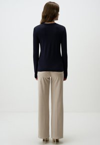 Maglione lungo blu navy con silhouette aderente, abbinato a pantaloni beige a gamba larga. Texture liscia e scollo rotondo, dettagli minimali.