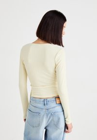 Lys gul langærmet top med en struktureret ribbet design, der har en rund halsudskæring og en tætsiddende silhuet, parret med lyseblå jeans.