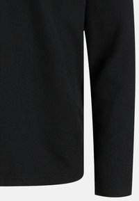 Camicia nera a maniche lunghe con una fine trama a coste mostrata dalla metà del busto al polso su uno sfondo neutro.