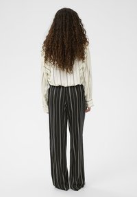 Svetlo prugasta krema bluza v kombinaciji z visokim pasom črnimi hlačami z vertikalnimi belimi črtami. Outfit ima sproščen, tekoč kroj.