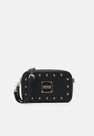 Bolso de bandolera rectangular negro con tachuelas doradas, correa ajustable, cierre de cremallera y placa con el logo dorado de Versace Jeans Couture en el centro.