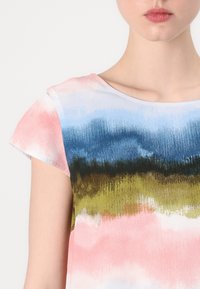 Kortermet topp med gradientmønster i pastellfarger: rosa, blå, grønn og brun. Mykt stoff med rund hals.