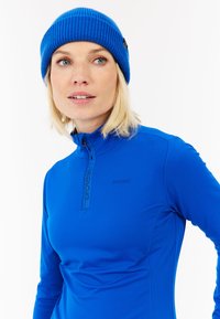 Plava jakna s punim zatvaračem i dugim rukavima, izrađena od glatkog materijala, s visokim ovratnikom i malim logotipom. Uparena s odgovarajućom pletenom kapom s rebrastim uzorkom.