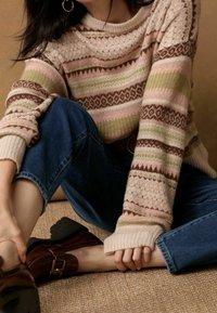 Pull en tricot avec des rayures horizontales dans des motifs rose, vert et marron ; associé à un jean bleu et des chaussures à talons marron.