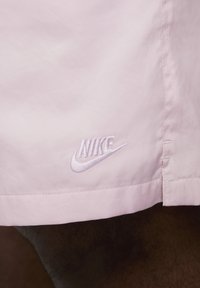 Shorts Nike rose clair présentant un léger éclat, une texture lisse et un logo brodé en bas à gauche.