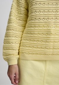 Jersey amarillo de punto con un patrón de rayas texturizadas y recortes florales. Presenta puños y dobladillo acanalados, combinado con una falda amarilla a juego.