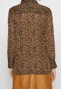 Camicia con stampa leopardata in tessuto leggero e trasparente. Presenta maniche lunghe, colletto a punta e orlo dritto. I motivi marroni e neri predominano.