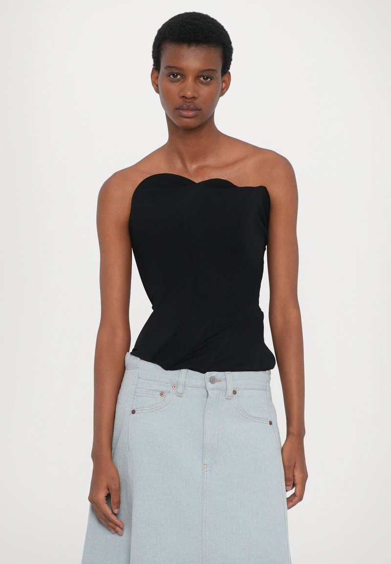 Schwarzes trägerloses Oberteil mit wellenförmigem Ausschnitt und gerafftem Stoffdesign, kombiniert mit einem hellblauen Jeansrock und hellen Messingakzenten.