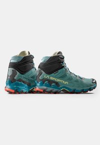 Scarpe outdoor alta in teal e nero con superfici testurizzate, accenti gialli e una suola robusta dotata di battistrada pronunciato per una buona aderenza.