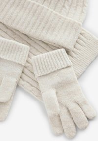 Guantes y gorro de color crema de punto, con puños acanalados y un patrón texturizado, hechos de una suave mezcla de lana.