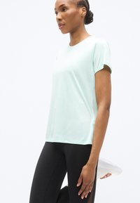 Αθλητική μπλούζα ανοιχτού μέντας με κοντά μανίκια, λεία υφή και πλευρικές χαραγές, σε συνδυασμό με μαύρα κολάν.