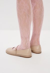 Beige ballerinat kengät pyöreällä kärjellä ja pienellä hihnalla, yhdisteissä läpikuultavien vaaleanpunaisten kalastajaverkko sukkahousujen kanssa, joissa on pitsimäinen kuvio.