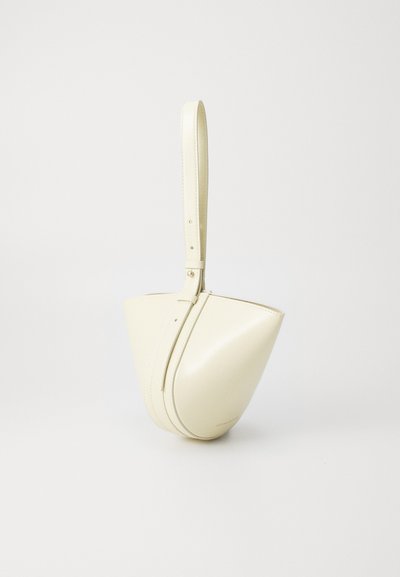 Balta ādas rokassoma ar unikālu izliekumu formu, ar garu siksnu un smalkiem izšuvuma elementiem. Gluda tekstūra, minimālisma dizains.