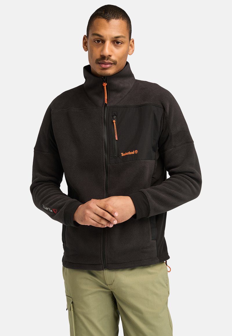 Giacca in pile nera con zip arancione, dotata di tasca sul petto e polsini elasticizzati. Include il logo Timberland sul davanti.