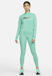 Maglietta verde menta a maniche lunghe con logo Nike Air, abbinata a leggings coordinati. Il tessuto sembra liscio e aderente, con un design senza cuciture.