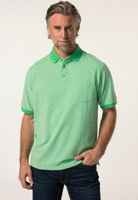 Grünes Polo-Shirt mit strukturiertem Muster, kontrastierendem Kragen und Ärmelabschlüssen in einem dunkleren Grünton sowie einer Brusttasche. Kombiniert mit dunkelblauen Jeans.