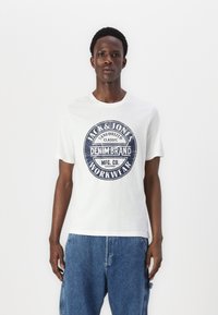 White cotton t-shirt featuring a round graphic print in navy with text: "JACK & JONES SANFORIZED CLASSIC DENIM BRAND MFG. CO. WORKWEAR."