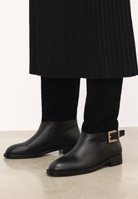 Black ankle boots made of smooth leather and soft suede, featuring a square buckle accent and a slightly stacked sole.