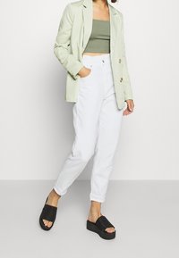Světlě zelený blazer, olivový crop top, bílé kalhoty s vysokým pasem a černé platformové sandály s horizontálními pruhy. Hladká látka, volný střih.