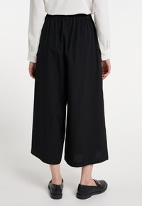 Zwarte wijde broek met een elastische tailleband, gemaakt van lichtgewicht stof, heeft een gladde textuur en valt net boven de enkel.