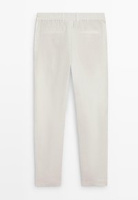 Pantalon slim ajusté de couleur blanc cassé avec taille élastique et deux poches passepoilées à l'arrière, présenté à plat de dos.