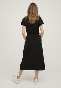 Vestido negro con un top de mangas cortas y una falda larga y suelta. La tela texturada presenta un patrón en cuadrícula. Combinado con zapatillas blancas.