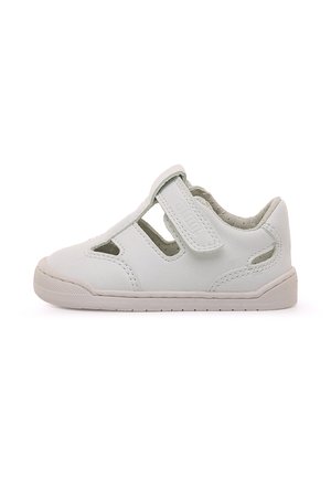 Chaussure pour enfants en cuir blanc avec motifs découpés, bride à Velcro et semelle flexible. Présente une surface texturée et un embout arrondi.