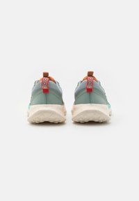 Scarpe sportive grigie con tomaia in rete testurizzata, dettagli arancioni e rossi, e suola di un beige chiaro maculato. Presentano linguette per un indossamento facile.