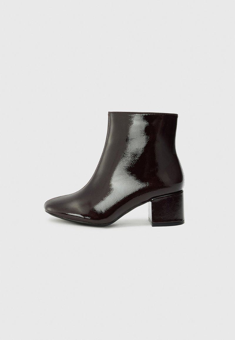 Botas de tobillo de charol negro con punta afilada y tacón grueso. Textura suave con un brillo sutil y líneas limpias, diseño minimalista.