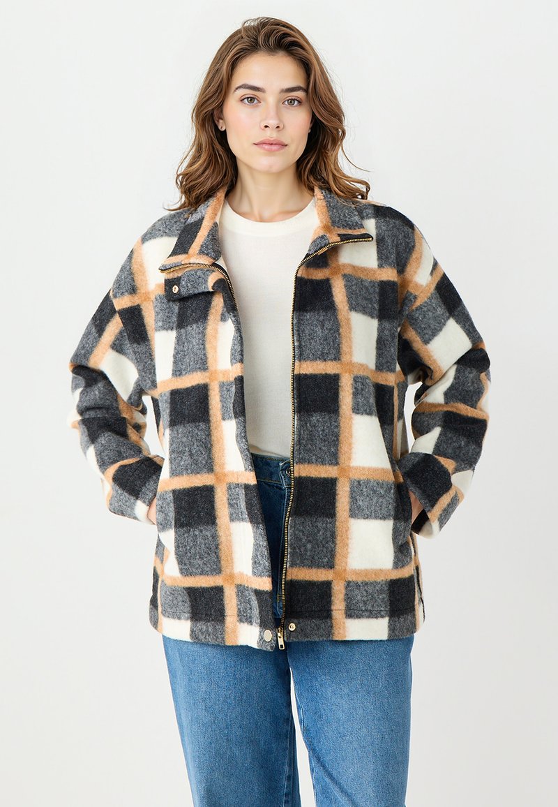 Fleece zip-up jack in een geruit patroon met zwarte, witte en oranje blokken. Voorzien van een staande kraag en twee zijzakken.