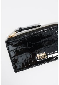 Cartera de charol negro con textura de cocodrilo, que presenta un logo dorado y un cierre de cremallera con un tirador negro.