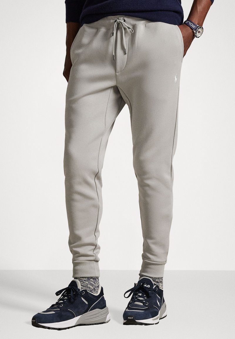Svetlo šedé jogger nohavice z mäkkého materiálu s elastickým pásom a šnúrkou, s bočnými vreckami a malým logom na nohavici.