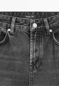 Jean en denim noir en gros plan montrant le bouton avant, les passants de ceinture, les poches et l'étiquette Massimo Dutti indiquant « Made in Turkey. »