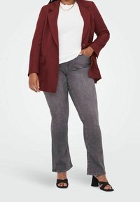 Blazer oversized burdeos sobre una blusa blanca, combinado con jeans acampanados grises y sandalias de tacón negras. Tejido texturizado con un cuello prominente.