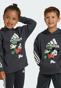 Felpe con cappuccio grigio scuro caratterizzate da una grande grafica di Topolino, tre strisce bianche sulle maniche e una texture del tessuto confortevole.