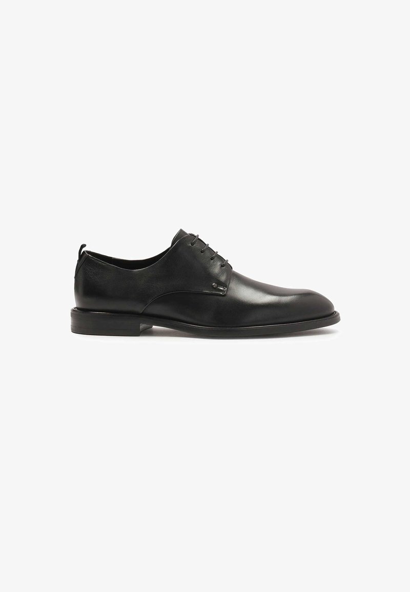 Chaussure habillée en cuir noir avec une finition lisse, bout arrondi, design à lacets et accents minimalistes. Semelle plate avec un léger talon.