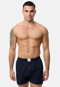 Marineblauwe boxershort gemaakt van katoen, met een elastische tailleband, een gulp aan de voorkant met rode knopen en een geweven label op de tailleband.