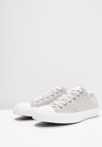 Grå kanvas sneakers med vit gummikappa, vita snören och silverfärgade öglor; låg design med textilmaterial och mönstrad sula.