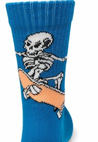 Calzino blu con uno scheletro bianco che cavalca uno skateboard arancione in una posa dinamica e in volo.