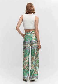 Top court blanc côtelé associé à un pantalon à jambes larges avec un motif paisley vert sur fond crème. Le pantalon a une taille haute.