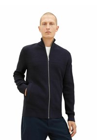 Sweat à zip bleu marine avec un design texturé, col montant, poignets côtelés et poches latérales. Fabriqué en tissu tricoté pour la chaleur et le confort.