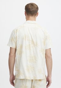 Short-sleeve, light cream shirt with beige palm tree pattern. Collar and relaxed fit, finished with side slits and a small brand tag.