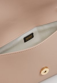 Růžová kabelka z umělé kůže s béžovou podšívkou, zdobená zlatým kováním a černou etiketou s nápisem "HUGO HUGO BOSS".