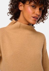Kamel-farbenes geripptes Sweater mit hohem Kragen und weicher Textur. Verfügt über vertikale Streifen und ein lässiges Design.