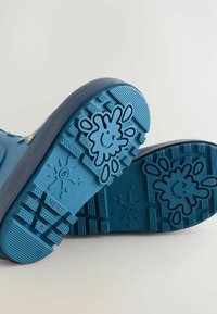 Zoccoli in gomma blu con suole texturizzate, dotati di un design vivace a schizzi e modelli scanalati per grip e stabilità.