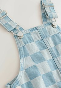 Blåternede denim overalls med sølvfarvede justerbare clips, der har en tekstureret overflade og kontrasterende lysere firkanter.
