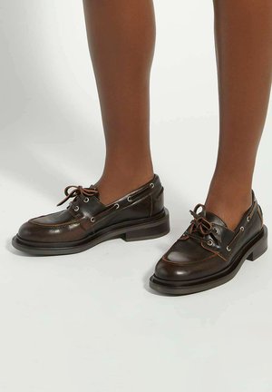 Brown leather shoes with rounded toe, contrast stitching, side lacing, and rubber sole, featuring grommets for laces and a low heel.