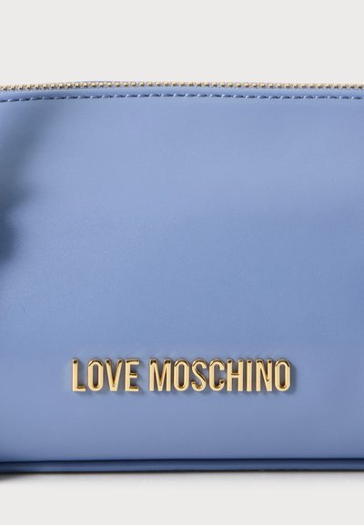Крупен план на светлосиня дамска чанта Love Moschino с релефни златни букви и златна верижка по горния ръб.
