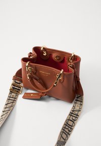 Brązowa skórzana torebka Emporio Armani z złotymi elementami, czerwonym wnętrzem i beżowym regulowanym paskiem z czarnym napisem logo Emporio Armani.